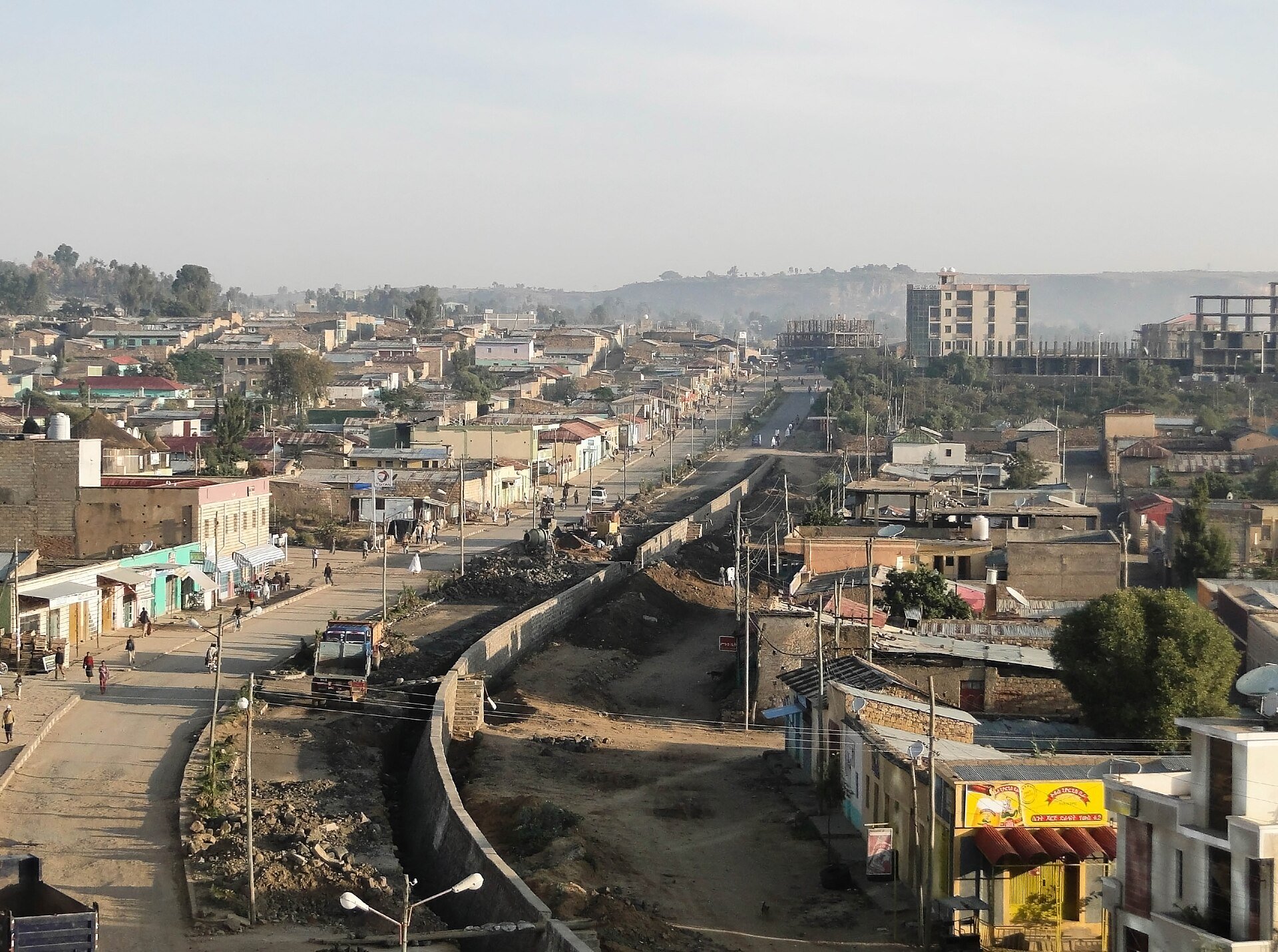 A view over the town of Adigrat in Ethiopia's Tigray region: a main street lined with low buildings, a road under construction in the foreground and hills in the distance.