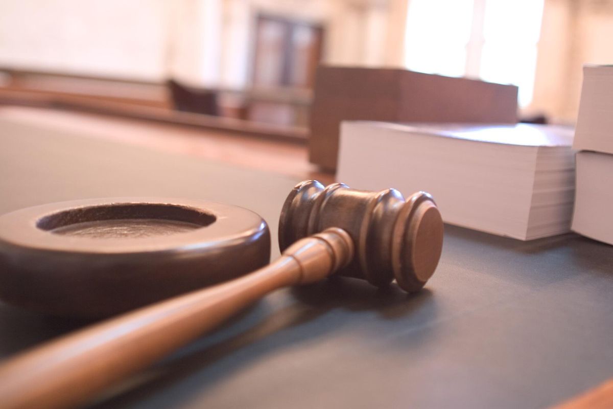 A wooden gavel and sound block on a courtroom bench beside stacks of law books.