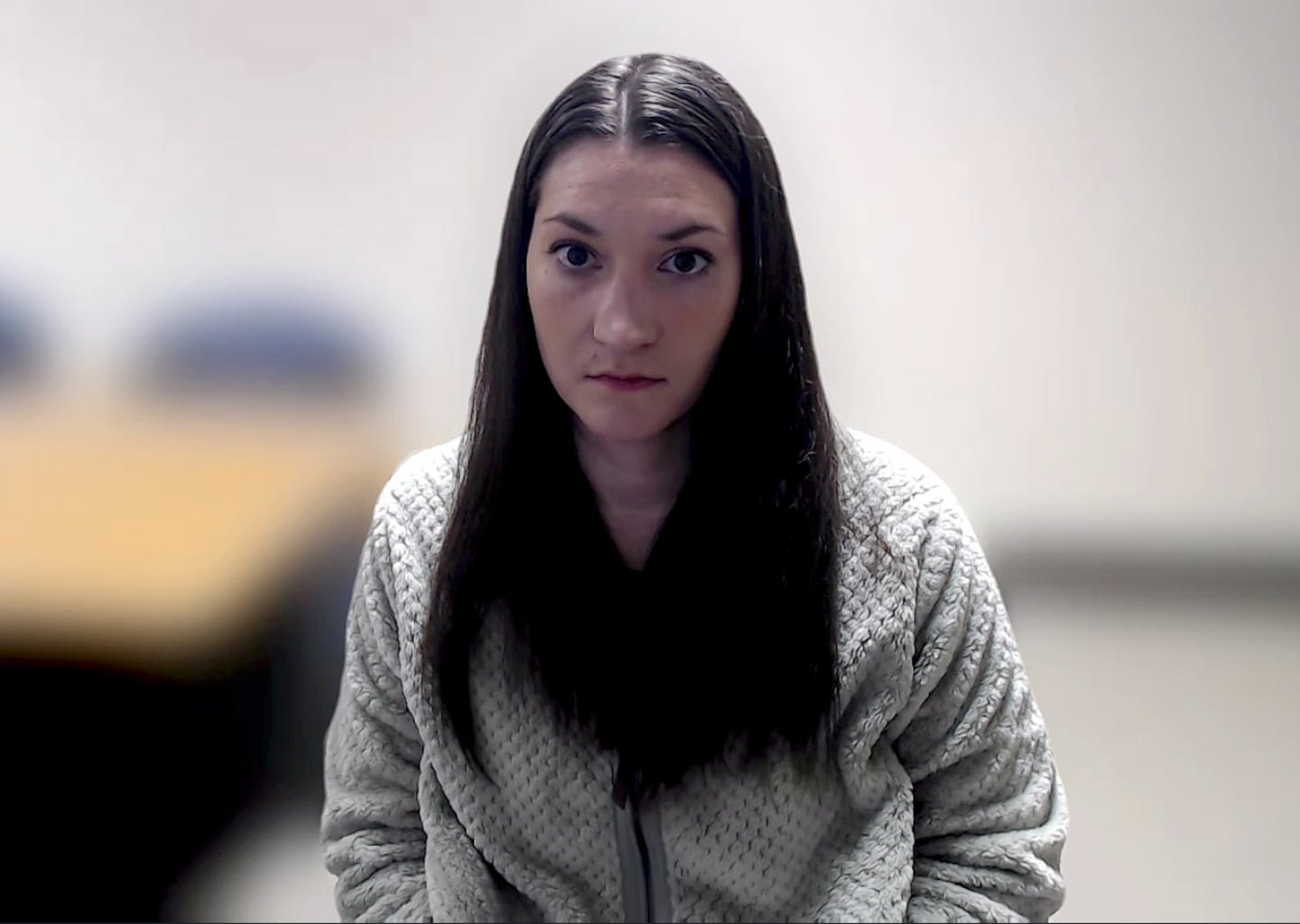 Lindsay Clancy, a woman with long dark hair wearing a gray fleece jacket, looks into the camera during a video court hearing.