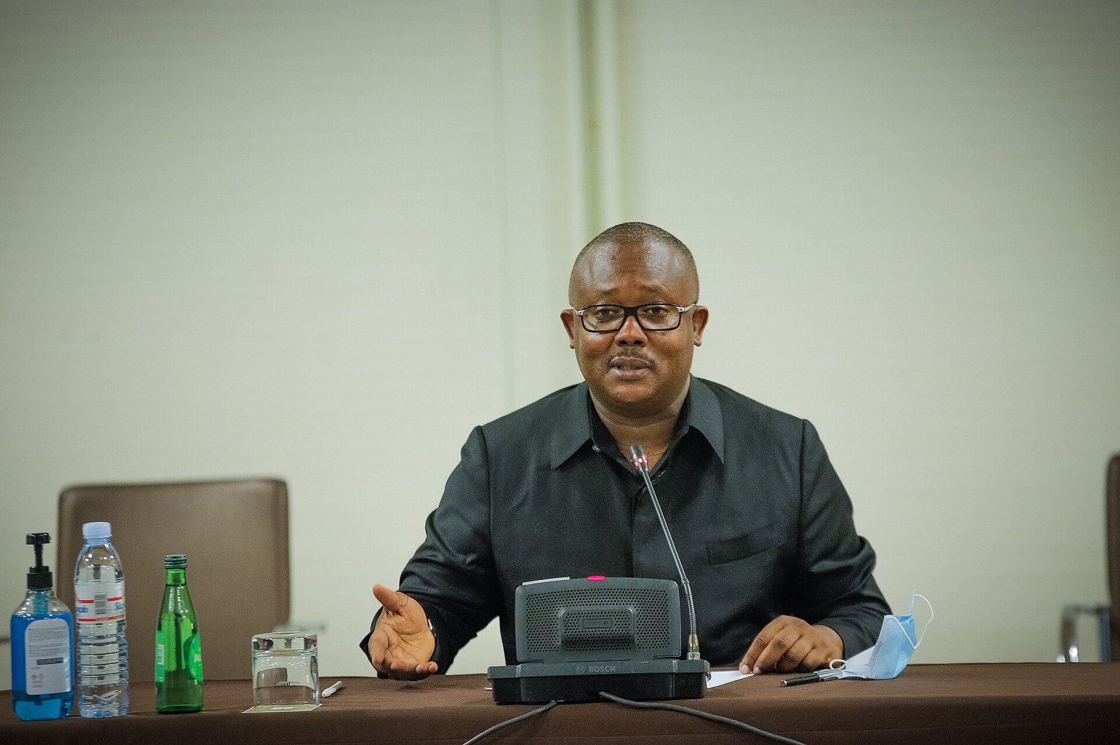 Umaro Sissoco Embaló in a dark shirt speaks at a table and gestures with one hand, with a microphone in front of him and a face mask beside it.